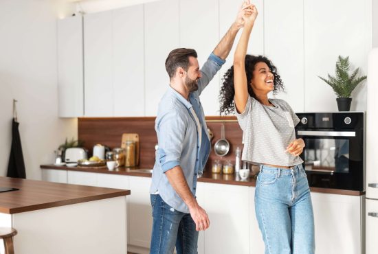 Romantic interracial couple dancing in the kitchen Handsome white man and attractive African American young woman is cooking and having fun together while cooking on the kitchen, romantic interracial couple is dancing while preparing lunch or dinner